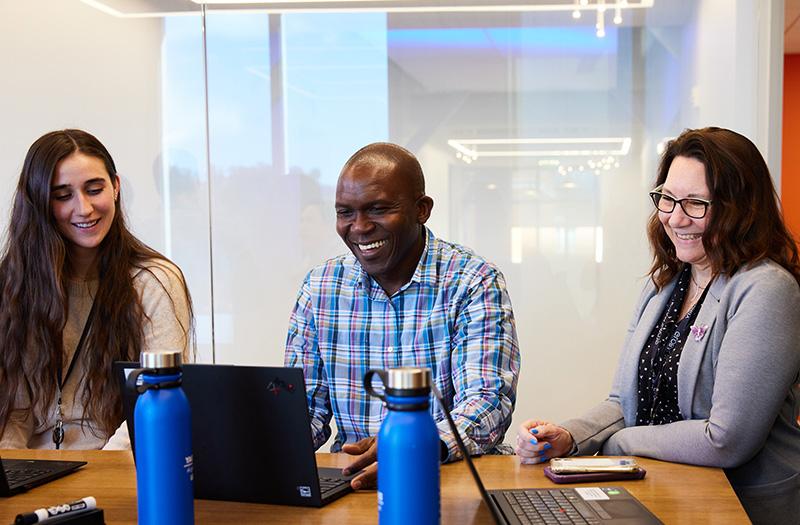 Three employees around a table looking at a computer.